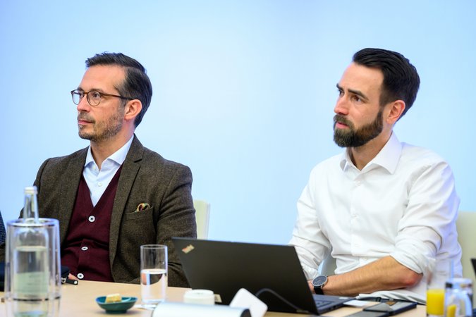 Öffnet eine Lightbox: Zwei Männer hören zu 