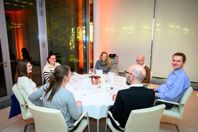 Öffnet eine Lightbox: Verschiedene Teilnehmer sitzen fröhlich am Tisch 